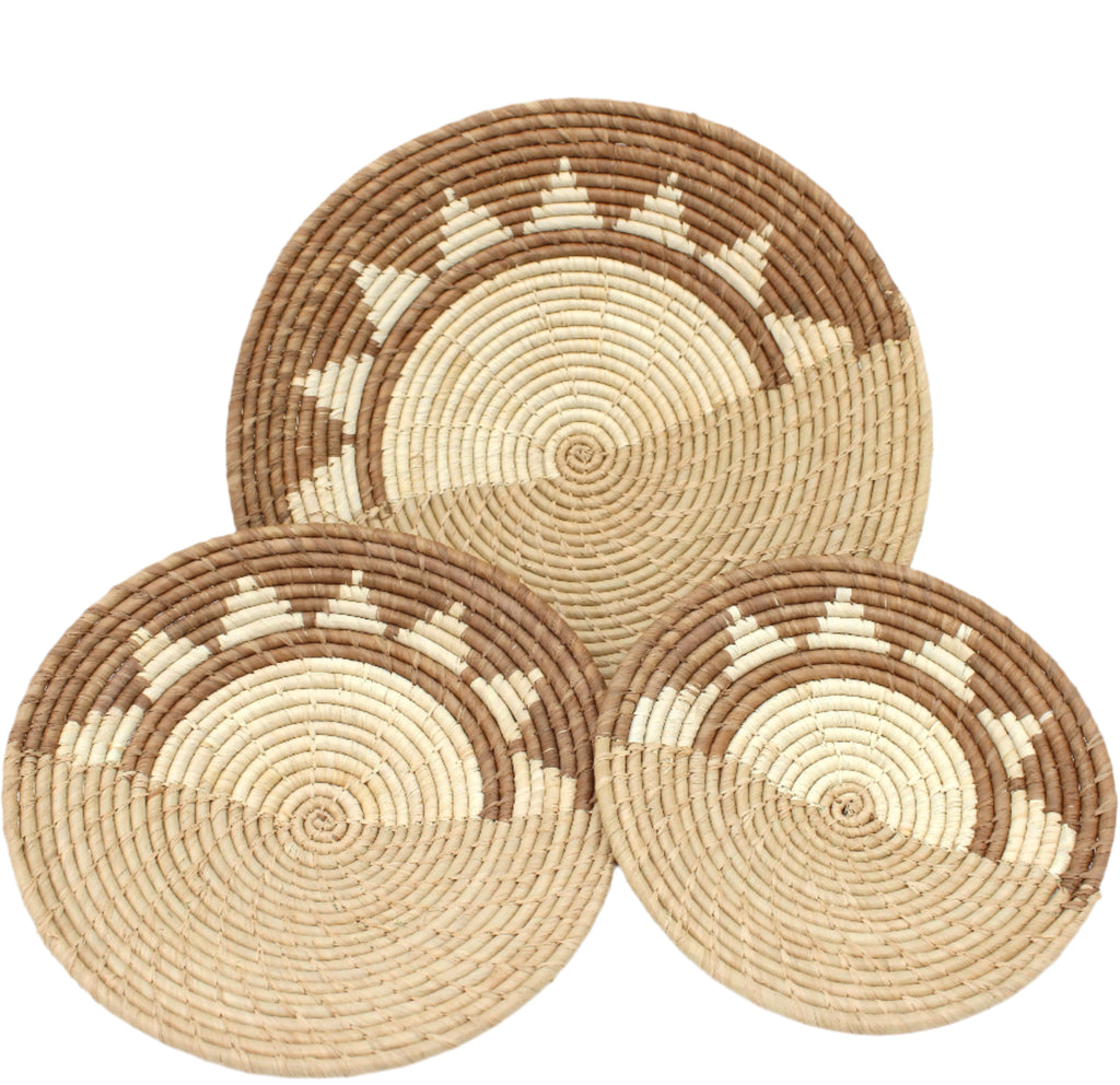 Dakarai Raffia Straw Wall Decor Display Basket Trays: Set of 3 handmade woven raffia palm fiber in a crochet loop technique creating a concentric swirl pattern of bands of  cinnamon/tobacco/brown, cappuccino/tea/light brown, and natural straw color that create a two tone pattern with half of the disc being light brown, and the other half a sun burst pattern set of three sized flat bowl trays - Shebobo