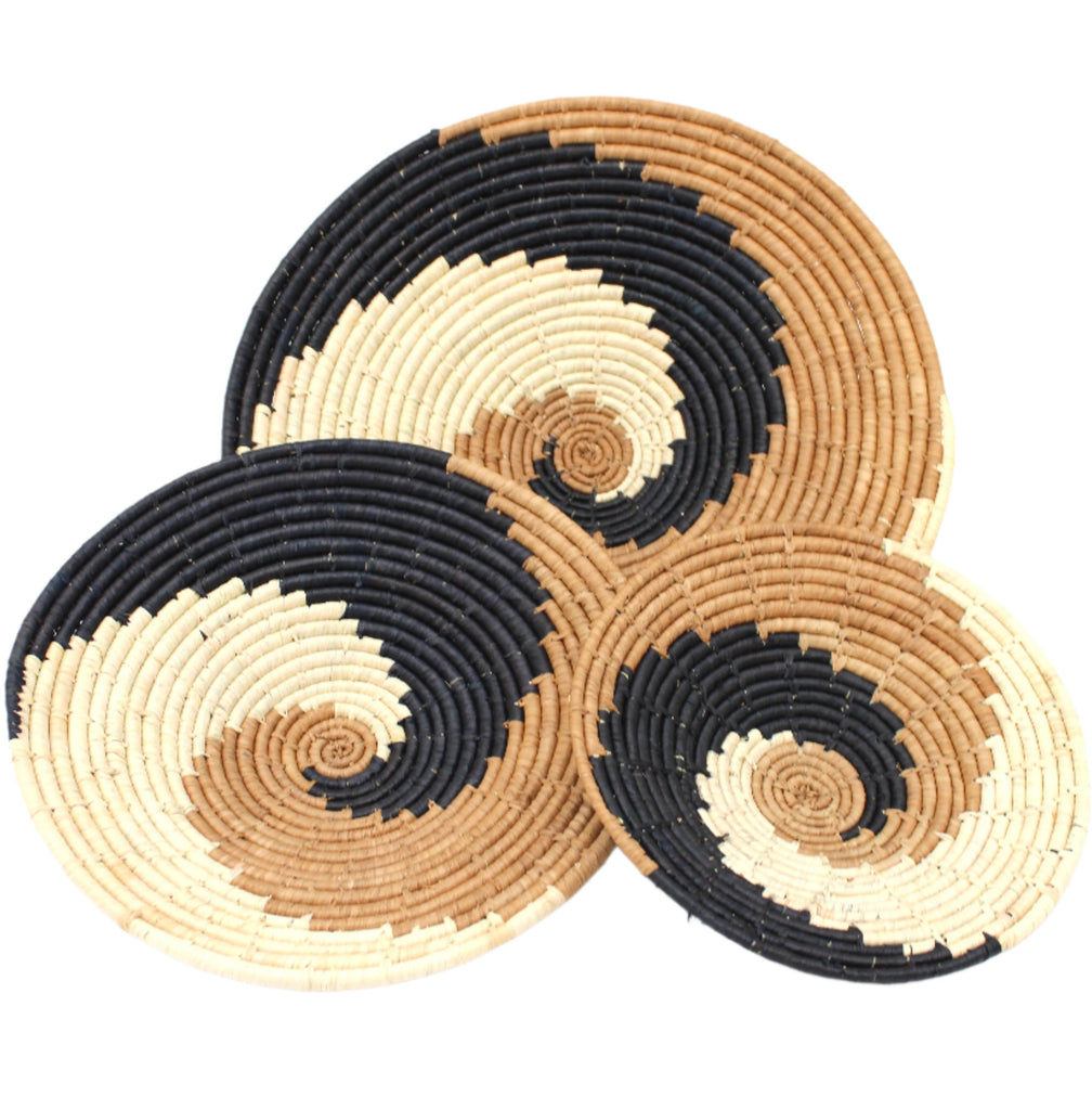 Dakarai Raffia Straw Wall Decor Display Basket Trays: Set of 3 handmade woven raffia palm fiber in a crochet loop technique creating a concentric swirl pattern of bands of natural straw color, cinnamon/tobacco/brown, and black in a three tone spiral from the center to the outer edge set of three sized flat bowl trays - Shebobo