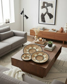 Lifestyle view Dakarai Raffia Straw Wall Decor Display Basket Tray: Set of 3 handmade woven natural raffia palm fiber in a crochet loop technique concentric coiled circular pattern with natural straw color, cappuccino/tea/light/brown, cinnamon/tobacco/dark/brown, and black centered star flower pattern set of three sized flat bowl trays - Shebobo