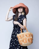 Model wearing Eva Embroidered Flower Crochet Straw Basket Handbag two tone handmade crochet raffia palm in a solid hue of natural straw color with blush pink/orange embroidered floral pattern and matching blush crochet handles beach bag tote purse - Shebobo (with Monica 5" & 7" Wide Brim Solid Color Packable Straw Sun Hats)