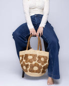 Model wearing Eva Embroidered Flower Crochet Straw Basket Handbag two tone handmade crochet raffia palm in a solid hue of natural straw color with Tobacco dark/cinnamon/brown embroidered floral pattern and matching blush crochet handles beach bag tote purse - Shebobo
