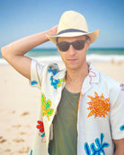 Model wearing Fedra Natural with Black Hat Band - Unisex Fedora Straw Hat handmade loomed natural raffia palm fiber in a solid hue of natural straw color with an attached black hat band - Shebobo