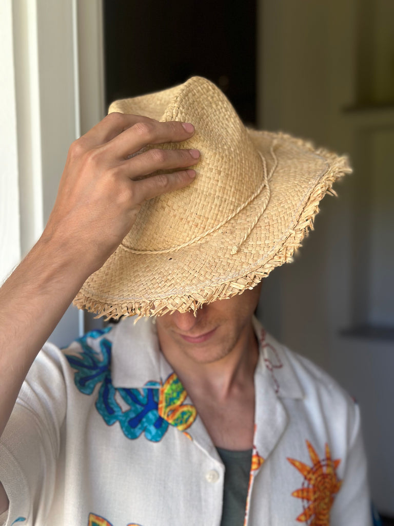 Model wearing Fiston Fringe Natural - Unisex Fedora Straw Hat with Raw Edge handmade woven raffia strands in a solid hue of natural straw color with matching raw fringe edge embellishment and twisted raffia cord hat band - Shebobo