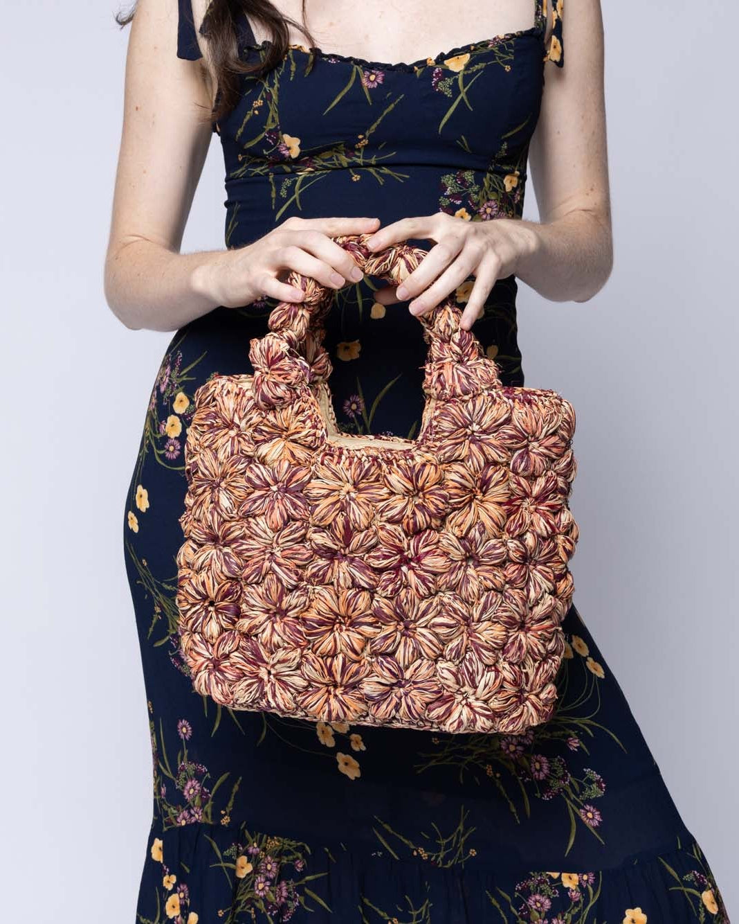 Model wearing Florence Umberwine Burgundy Reds Multicolor Flower Crochet Straw Basket Handbag handmade natural raffia palm fiber in a multicolor hue combination of natural straw color, umberwine burgundy/claret/bordeaux/dark/red/purple, and blush orange/pink with subtle tied flower design consisting of 88 flowers crochet together along the outside of the bag as well as the handles purse tote - Shebobo