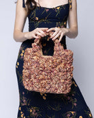 Model wearing Florence Umberwine Burgundy Reds Multicolor Flower Crochet Straw Basket Handbag handmade natural raffia palm fiber in a multicolor hue combination of natural straw color, umberwine burgundy/claret/bordeaux/dark/red/purple, and blush orange/pink with subtle tied flower design consisting of 88 flowers crochet together along the outside of the bag as well as the handles purse tote - Shebobo