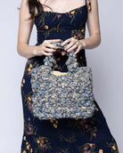 Model wearing Florence Denim Blues Multicolor Flower Crochet Straw Basket Handbag handmade natural raffia palm fiber in a multicolor hue combination of natural straw color, denim light/retro/blue, and luminous navy/dark/blue with subtle tied flower design consisting of 88 flowers crochet together along the outside of the bag as well as the handles purse tote - Shebobo