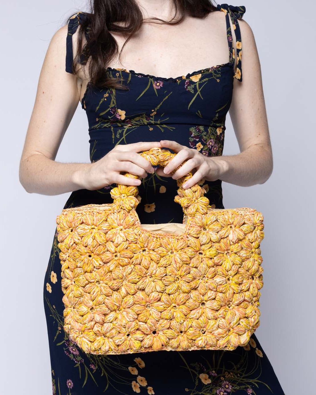 Model wearing Florence Lemon Yellows Multicolor Flower Crochet Straw Basket Handbag handmade natural raffia palm fiber in a multicolor hue combination of natural straw color, lemon yellow, and orange with subtle tied flower design consisting of 88 flowers crochet together along the outside of the bag as well as the handles purse tote - Shebobo