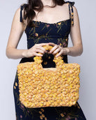 Model wearing Florence Lemon Yellows Multicolor Flower Crochet Straw Basket Handbag handmade natural raffia palm fiber in a multicolor hue combination of natural straw color, lemon yellow, and orange with subtle tied flower design consisting of 88 flowers crochet together along the outside of the bag as well as the handles purse tote - Shebobo