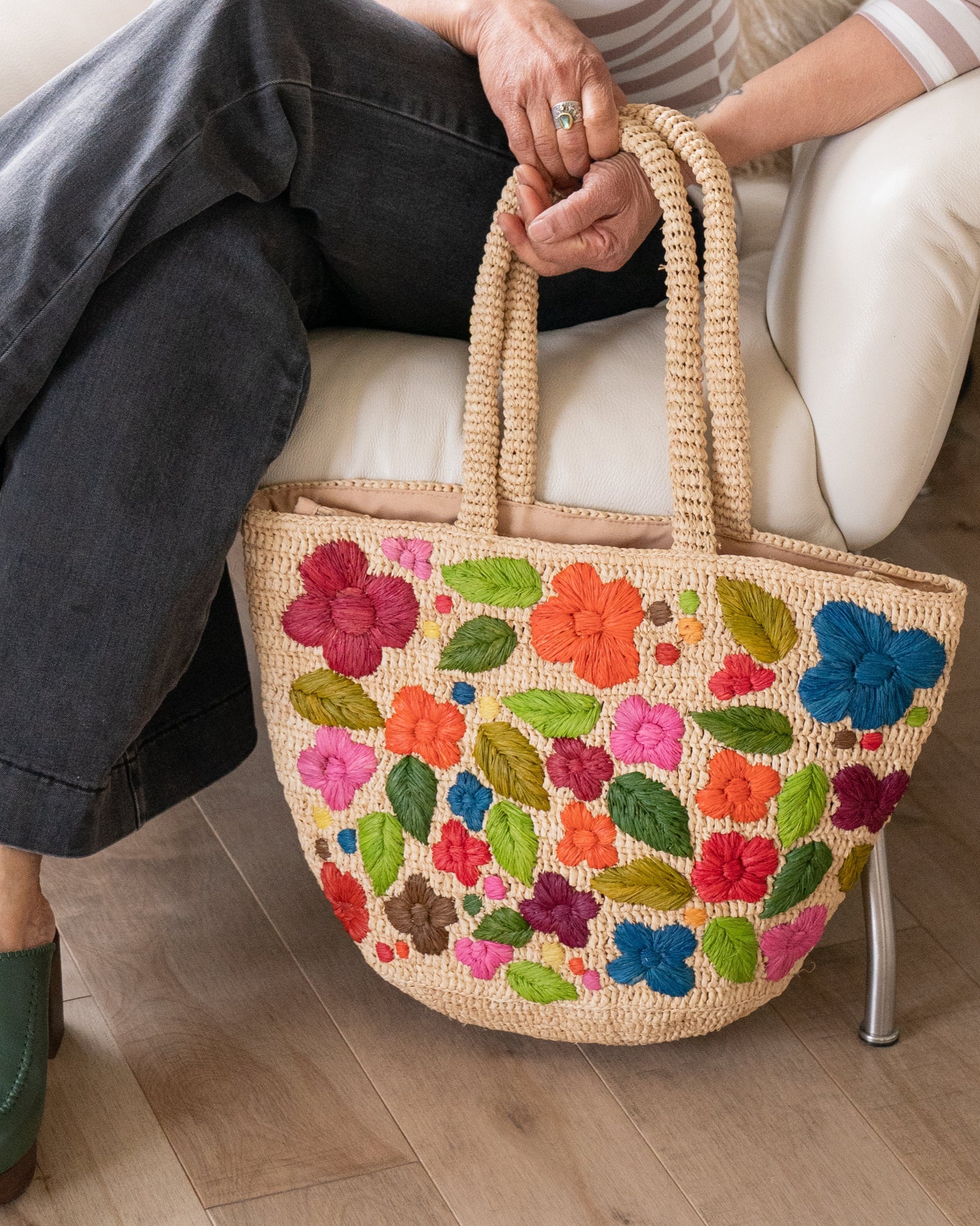 Model wearing Full Bloom Crochet Straw Handbag with Embroidered Flowers handmade natural raffia palm fiber in a solid hue of natural straw color with subtle horizontal banded link texture and multicolor embroidered detailing in fuchsia hot/bright/barbie/pink, light pink, red, coral orange/red, orange, dark chocolate brown, cinnamon/tobacco/dark/brown, dusk navy/dark/blue, green, olive green, lime green, yellow, purple, etc. colored flowers, leaves and dots embellishment tote beach bag purse - Shebobo