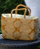 Lifestyle view Gemma Crochet Disc Rectangle Butter and Saffron Straw Basket Handbag handmade woven raffia palm fiber in a two tone multicolor pattern of butter light yellow and saffron yellow/orange create a coiled braid disc pattern result in a star pattern around the bag with matching woven handles top handle bag - Shebobo