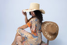 Model wearing 5.5" Brim Gigi Natural and Cinnamon Floral Embroidered Crochet Straw Sun Hats handmade crochet natural raffia palm fiber in a solid hue of natural straw color making a concentric pattern from the center top of the flattened crown spiraling out to the edge of the brim with matching adjustable raffia braid hat band and cinnamon dark brown floral pattern with leaves embroidered on the brim - Shebobo