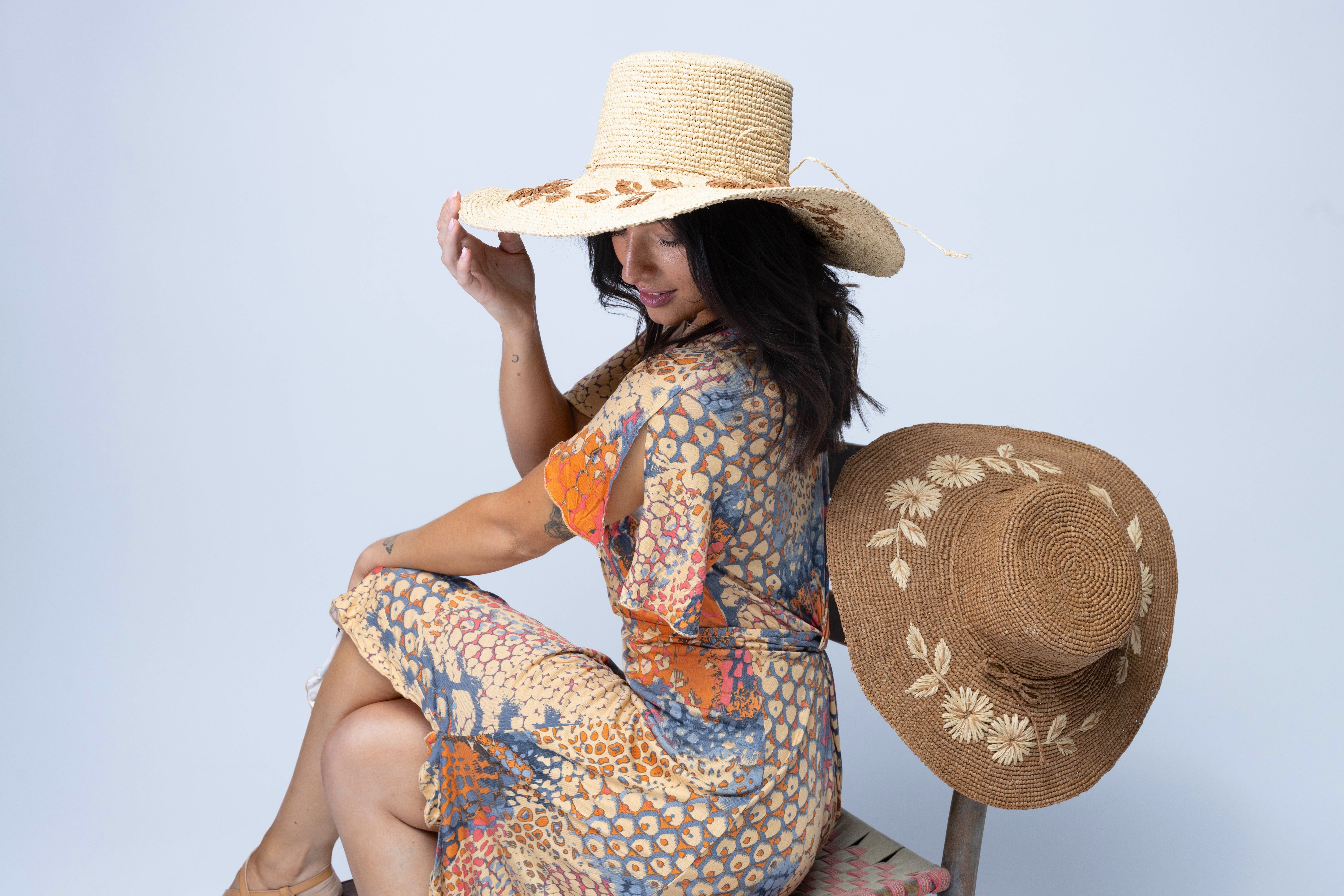 Model wearing 5.5" Brim Gigi Natural and Cinnamon Floral Embroidered Crochet Straw Sun Hats handmade crochet natural raffia palm fiber in a solid hue of natural straw color making a concentric pattern from the center top of the flattened crown spiraling out to the edge of the brim with matching adjustable raffia braid hat band and cinnamon dark brown floral pattern with leaves embroidered on the brim - Shebobo