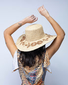 Model wearing 5.5" Brim Gigi Natural and Cinnamon Floral Embroidered Crochet Straw Sun Hats handmade crochet natural raffia palm fiber in a solid hue of natural straw color making a concentric pattern from the center top of the flattened crown spiraling out to the edge of the brim with matching adjustable raffia braid hat band and cinnamon dark brown floral pattern with leaves embroidered on the brim - Shebobo