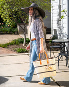 Model wearing Havana Sisal Basket Bag with Tassel Charm Embellishment handmade sisal fiber woven into horizontal wide bands of natural straw color with two evenly spaced narrow bands of black create a stripe pattern with matching crochet starfish charm embellishment and leather handles handbag shoulder bag - Shebobo (with 7" Wide Brim Natasha Woven Straw Sun Hat)