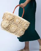 Model wearing Hearts Crochet Straw Basket Bag with Fringed Heart Pattern handmade woven raffia in a solid hue of natural straw color with granny square pattern and raised/stuffed heart pattern with fringe edges on each heart, looped base and top binding, as well as leather handles purse beach bag shoulder bag - Shebobo 