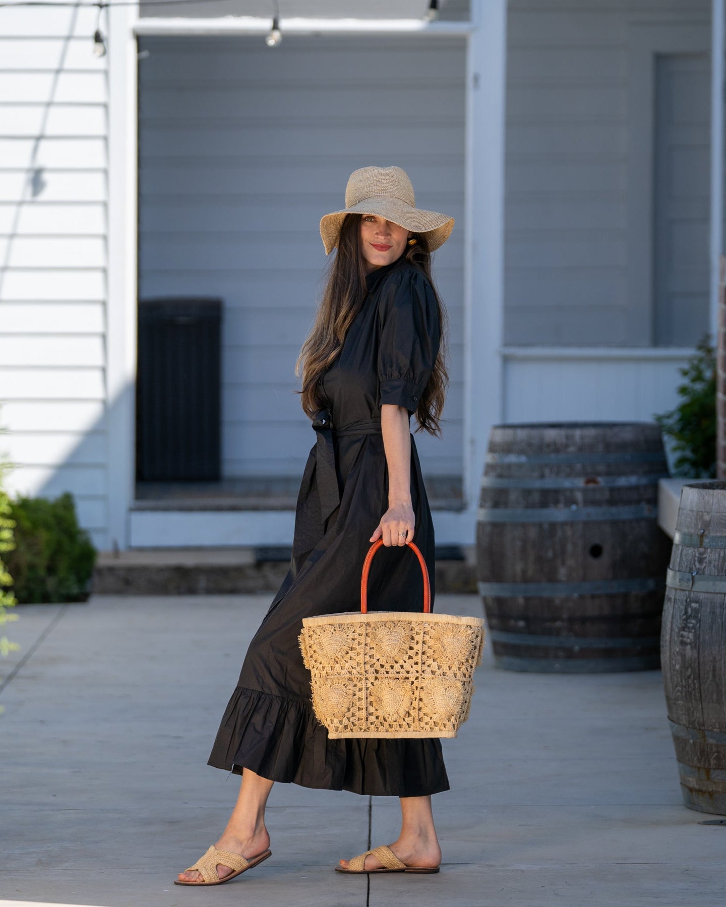 Model wearing Hearts Crochet Straw Basket Bag with Fringed Heart Pattern handmade woven raffia in a solid hue of natural straw color with granny square pattern and raised/stuffed heart pattern with fringe edges on each heart, looped base and top binding, as well as leather handles purse beach bag shoulder bag - Shebobo (with 3.5" Brim Crochet Miramar Straw Sun Hat and Lizzie Crochet Straw Sandals)