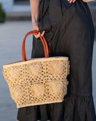Model wearing Hearts Crochet Straw Basket Bag with Fringed Heart Pattern handmade woven raffia in a solid hue of natural straw color with granny square pattern and raised/stuffed heart pattern with fringe edges on each heart, looped base and top binding, as well as leather handles purse beach bag shoulder bag - Shebobo 