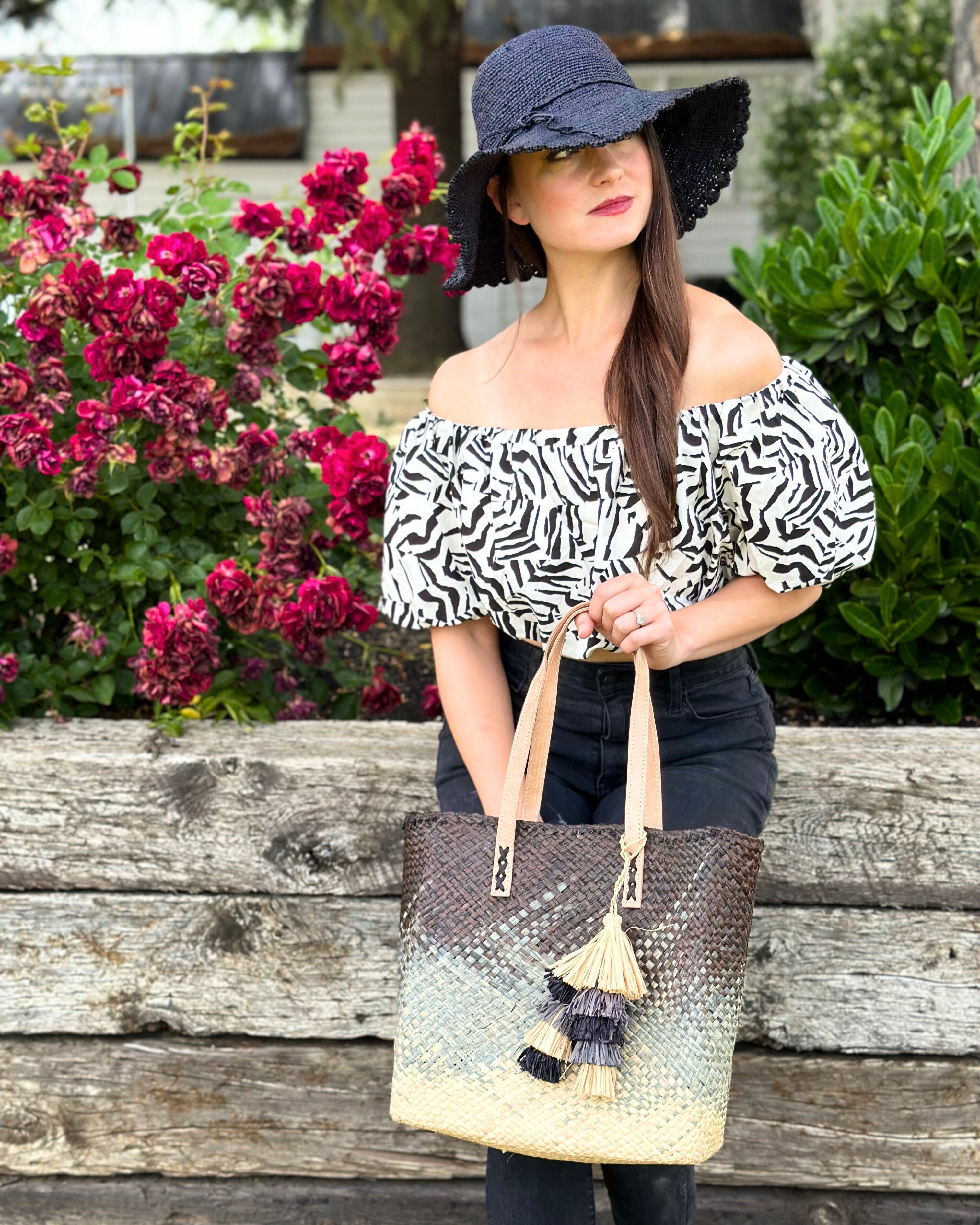 Model wearing Holden Ombre Black Straw Handbag Tassel Charm Embellishment handmade woven raffia dip dyed gradient of black, grey, and natural with matching multicolored, multi-tiered raffia tuft tassel with 4" Brim Genevieve Crochet Straw Sun Hats with Lace Weave Edge Black - Shebobo