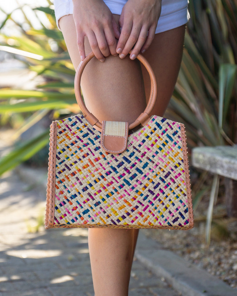 Model wearing Ibiza Confetti Multi Straw HandBag with Leather Handles handmade woven natural raffia fiber purse with multicolor natural, yellow, orange, pink, fuchsia, bordeaux, turquoise, etc.  crosshatch pattern and loomed sides with leather loop handles, woven leather side seam binding, and flap closure - Shebobo