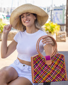 Model wearing Ibiza Raspberry Multi Straw HandBag with Leather Handles handmade woven natural raffia fiber purse with multicolor yellow, orange, pink, fuchsia, bordeaux, blue, turquoise, etc. crosshatch pattern and loomed sides with leather loop handles, woven leather side seam binding, and flap closure with 5" Wide Brim Natural Raffia Palm Packable Straw Hat - Shebobo