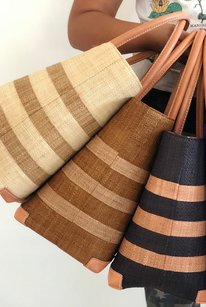 Model wearing Jacky Natural, Cinnamon/Tobacco, and Black Small Straw Basket Bags handmade loomed raffia palm fiber in one color with three centered horizontal stripes of tobacco/cinnamon/brown handbag purse with leather handles and detailing - Shebobo