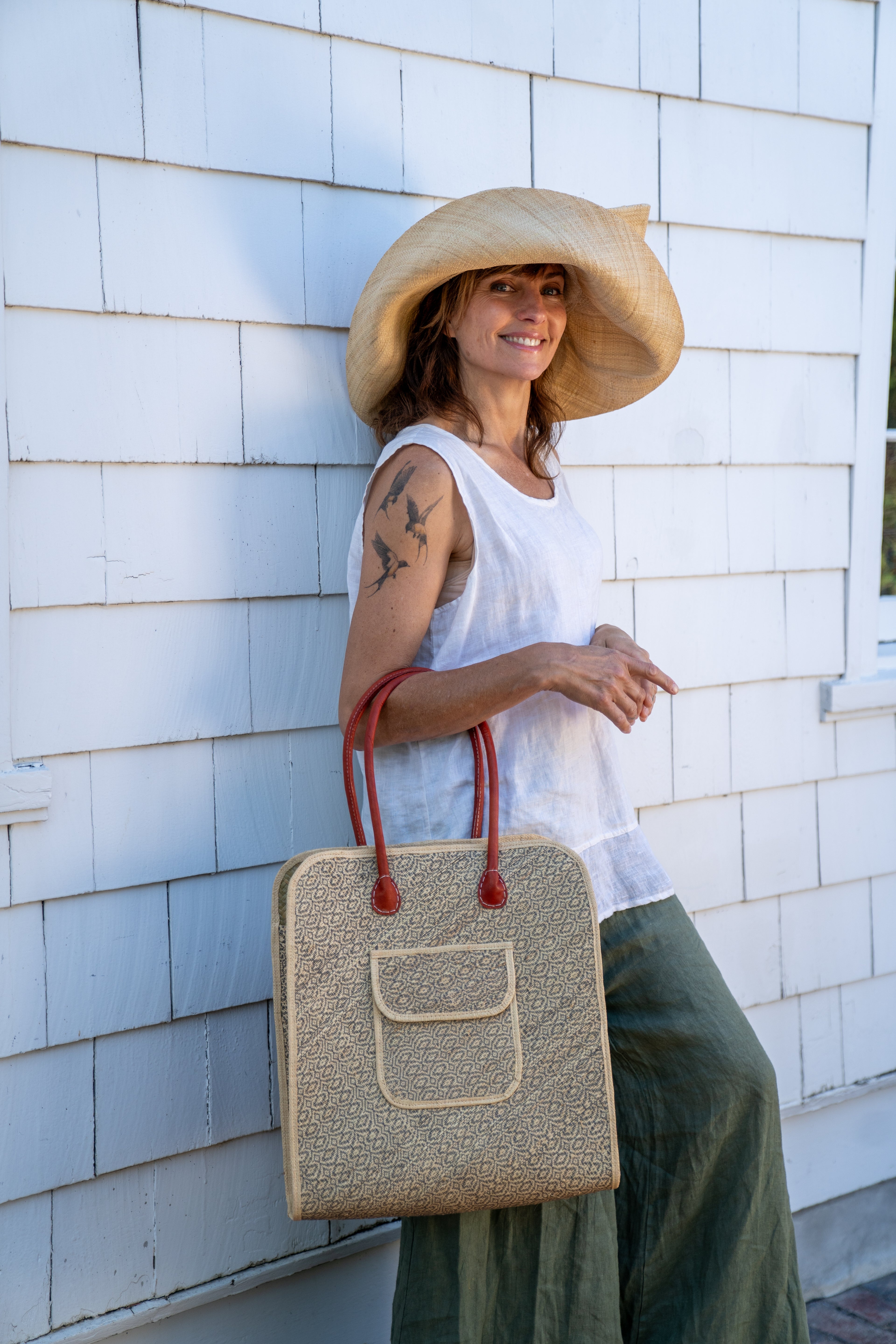 Model wearing Josephine 50's Inspired Woven Straw Handbag handmade natural raffia palm fiber in natural straw color woven with contrasting Grey thread stitching in a subtle diagonal stripe pattern consisting of bands of ovals and circles with loomed raffia edging around the bag as well as the pocket and flap of the exterior pocket - Shebobo (with Audrey 5" & 7" Wide Brim Big Bow Solid Color Packable Straw Sun Hats) 