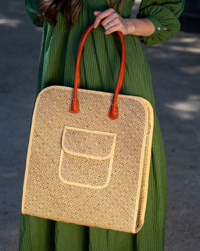 Model wearing Josephine 50's Inspired Woven Straw Handbag handmade natural raffia palm fiber in natural straw color woven with contrasting Black thread stitching in a subtle diagonal stripe pattern consisting of bands of ovals and circles with loomed raffia edging around the bag as well as the pocket and flap of the exterior pocket - Shebobo