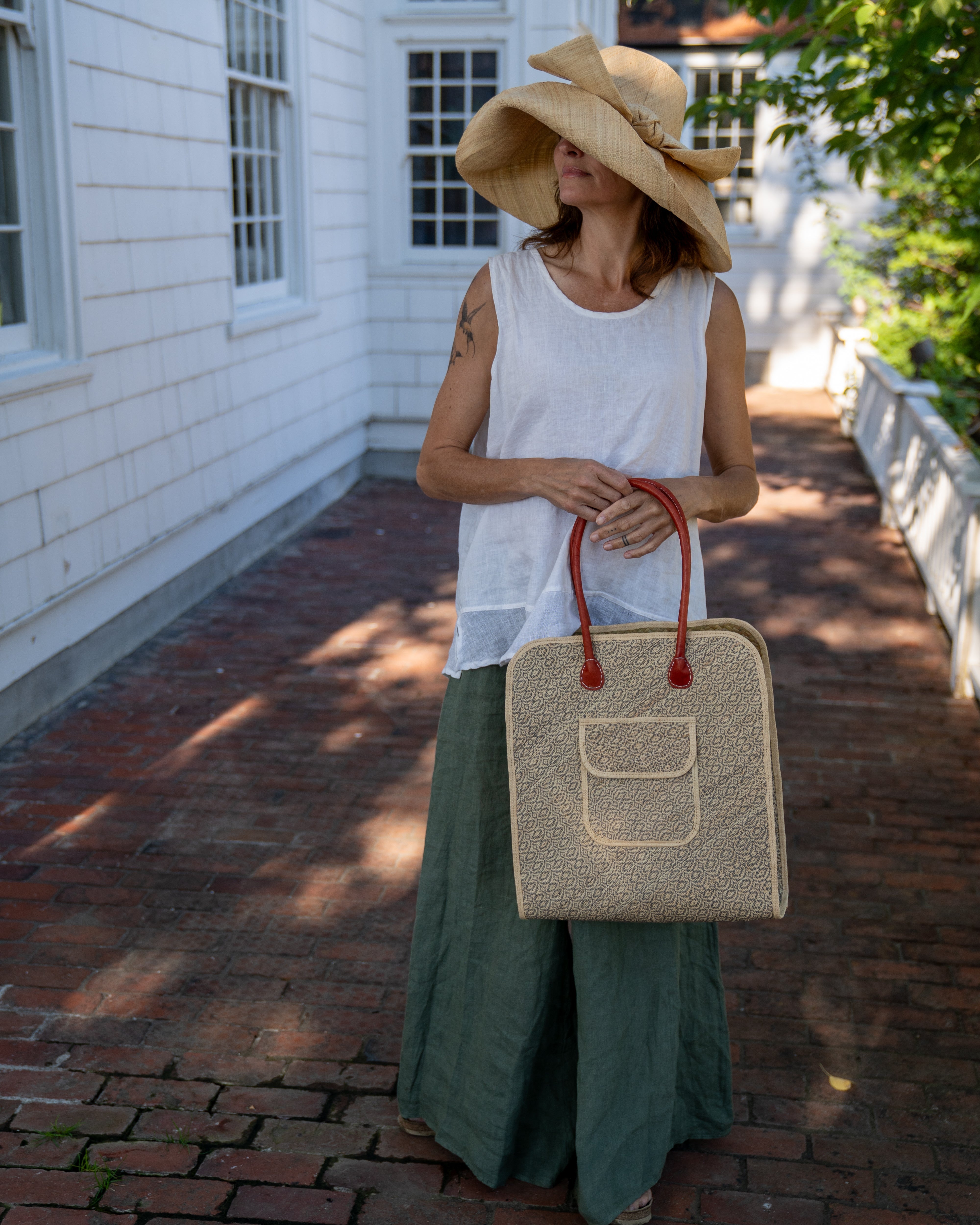 Model wearing Josephine 50's Inspired Woven Straw Handbag handmade natural raffia palm fiber in natural straw color woven with contrasting Grey thread stitching in a subtle diagonal stripe pattern consisting of bands of ovals and circles with loomed raffia edging around the bag as well as the pocket and flap of the exterior pocket - Shebobo (with Audrey 5" & 7" Wide Brim Big Bow Solid Color Packable Straw Sun Hats) 
