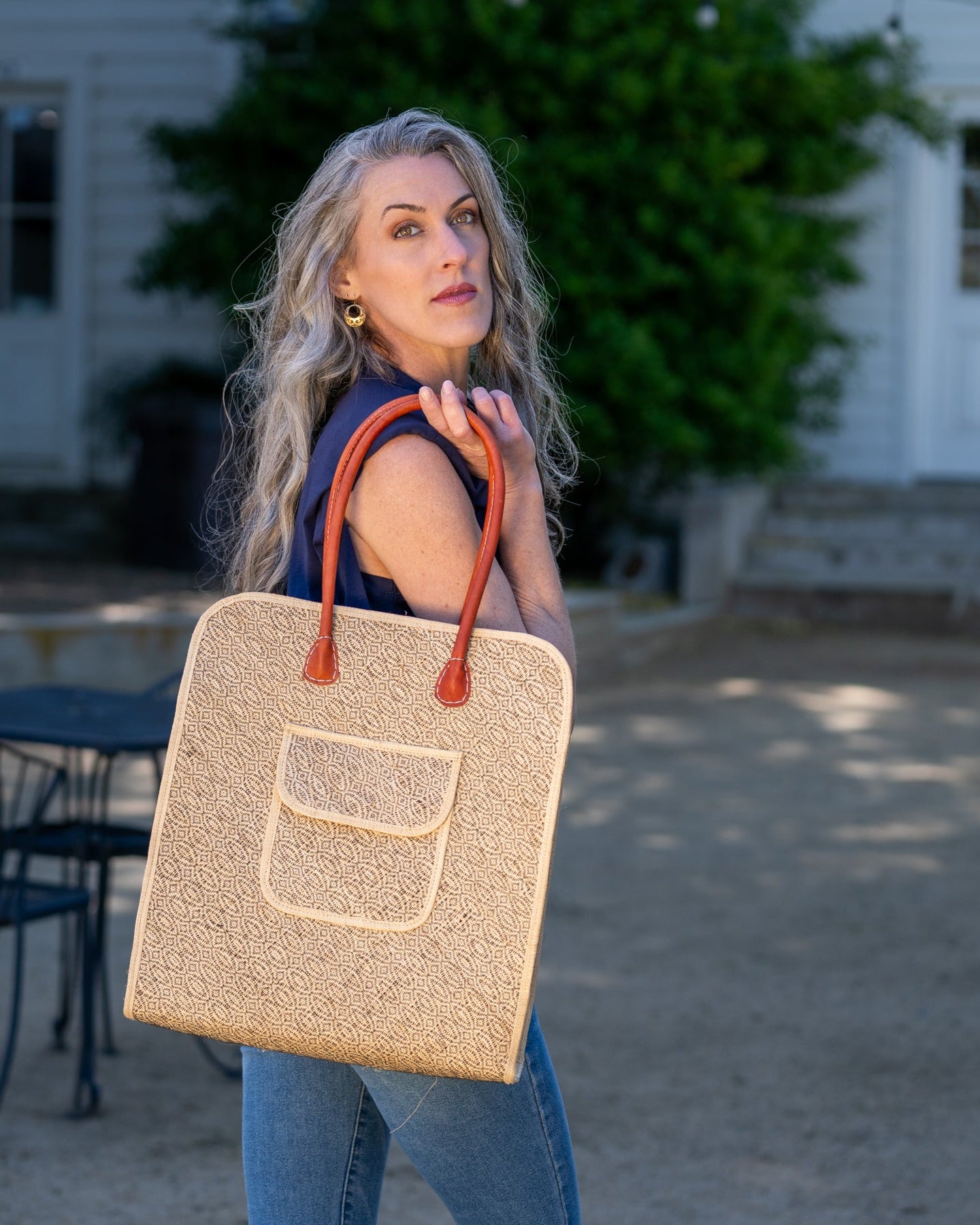 Model wearing Josephine 50's Inspired Woven Straw Handbag handmade natural raffia palm fiber in natural straw color woven with contrasting Black thread stitching in a subtle diagonal stripe pattern consisting of bands of ovals and circles with loomed raffia edging around the bag as well as the pocket and flap of the exterior pocket - Shebobo