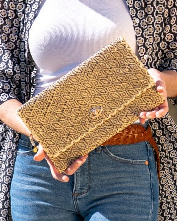 Model wearing Josephine Woven Straw Clutch Purse handmade natural raffia palm fiber in natural straw color woven with contrasting black thread stitching in a subtle diagonal stripe pattern consisting of bands of ovals and circles handbag with crosshatch stitch edging - Shebobo