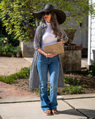 Model wearing Josephine Woven Straw Clutch Purse handmade natural raffia palm fiber in natural straw color woven with contrasting black thread stitching in a subtle diagonal stripe pattern consisting of bands of ovals and circles handbag with crosshatch stitch edging - Shebobo (with 7" Brim Natasha Woven XL Straw Sun Hats)