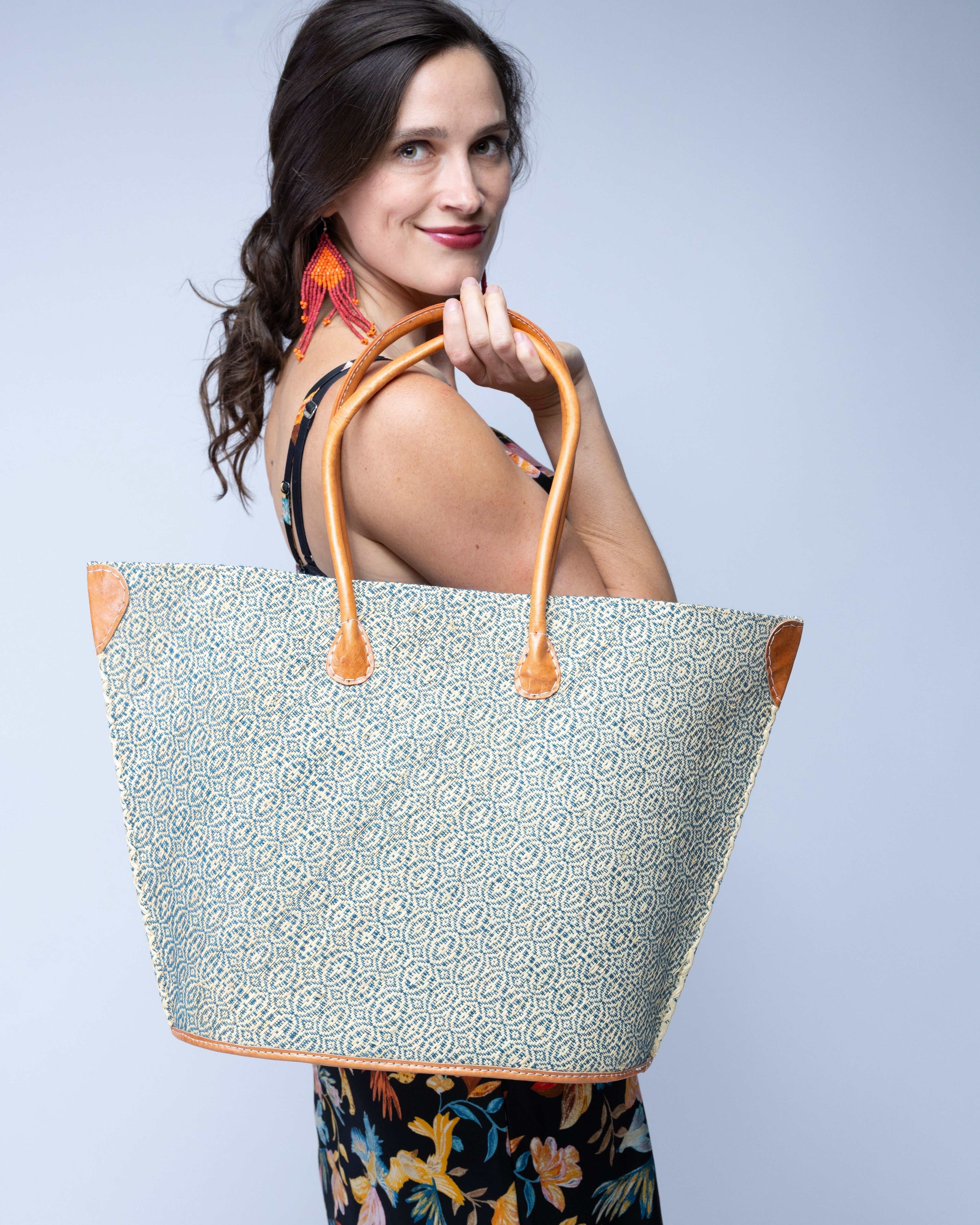 Model wearing Josephine Woven Small Straw Tote Bag handmade natural raffia palm fiber in natural straw color woven with contrasting Turquoise blue/green thread stitching in a subtle diagonal stripe pattern consisting of bands of ovals and circles with natural cross-stitch edge and leather handles beach bag shoulder bag - Shebobo