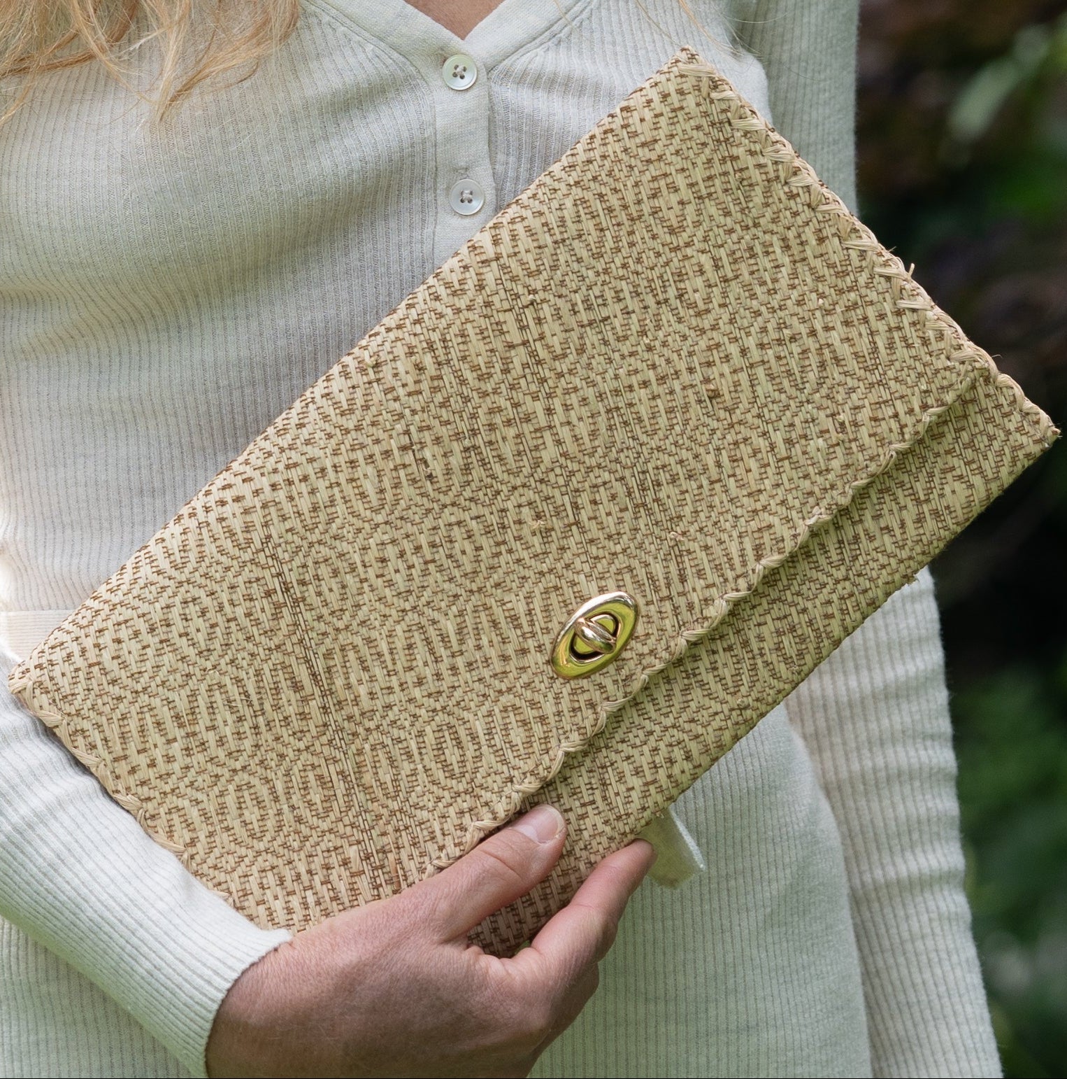 Model wearing Josephine Woven Straw Clutch Purse handmade natural raffia palm fiber in natural straw color woven with contrasting cinnamon tobacco/dark/brown thread stitching in a subtle diagonal stripe pattern consisting of bands of ovals and circles handbag with crosshatch stitch edging - Shebobo