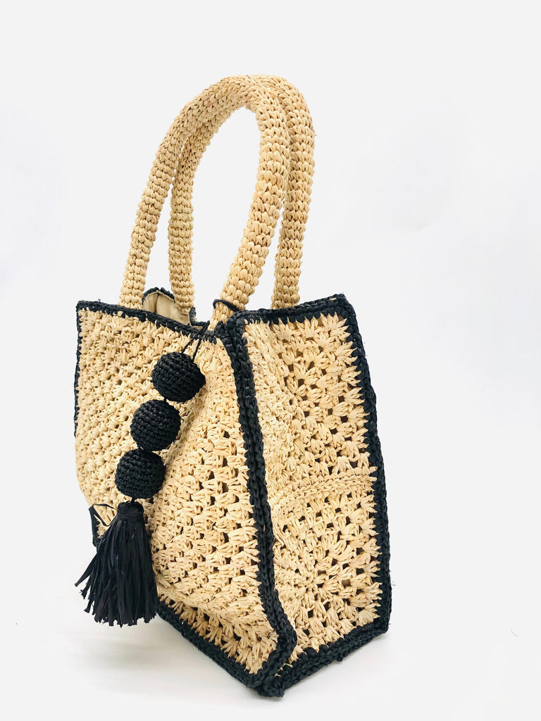 Side view Kimba handmade crochet two tone handbag purse natural straw color with black trim and crochet cascading balls plus tassel bag charm embellishment - Shebobo