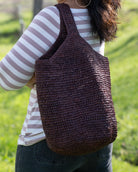 Model wearing Kiki Crochet Straw Crossbody Bag handmade natural raffia palm fiber in a crochet pattern of subtle linked bands in a solid hue of dark chocolate brown purse - Shebobo