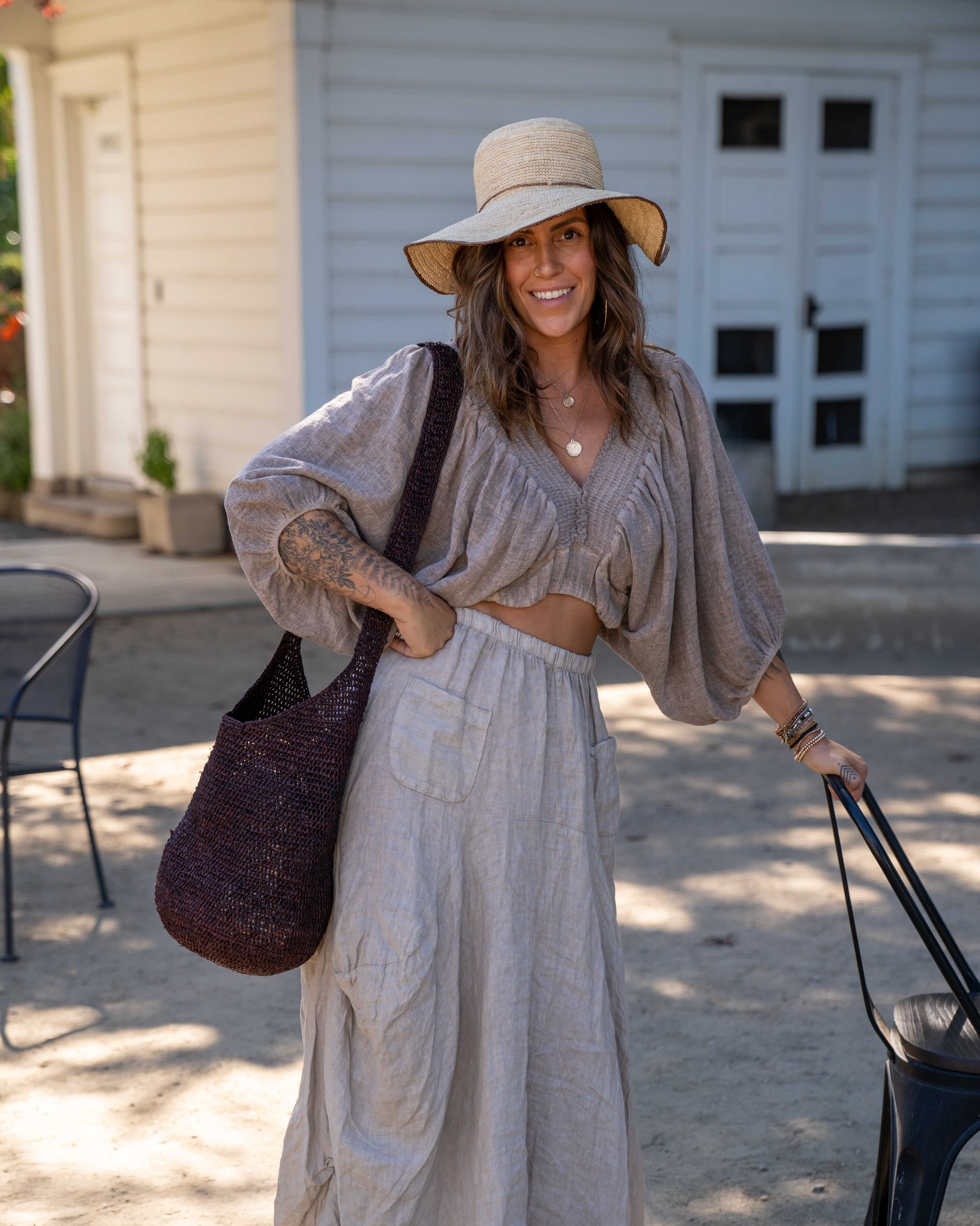 Model wearing Model wearing Kiki Crochet Straw Crossbody Bag handmade natural raffia palm fiber in a crochet pattern of subtle linked bands in a solid hue of dark chocolate brown purse - Shebobo (with Rachel 4" Brim Crochet Straw Sun Hats with Colored Edge)