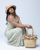 Model wearing Kiri Ruffle Crochet Straw Basket Handbag handmade crochet natural raffia palm fiber in a solid hue of natural straw color in subtle link texture with sweet double ruffle embellishment around the top of the bag and matching crochet handles beach bag shoulder bag - Shebobo (with Kate 3" Brim Crochet Bucket Straw Hats with Colored Lace Weave Edge)