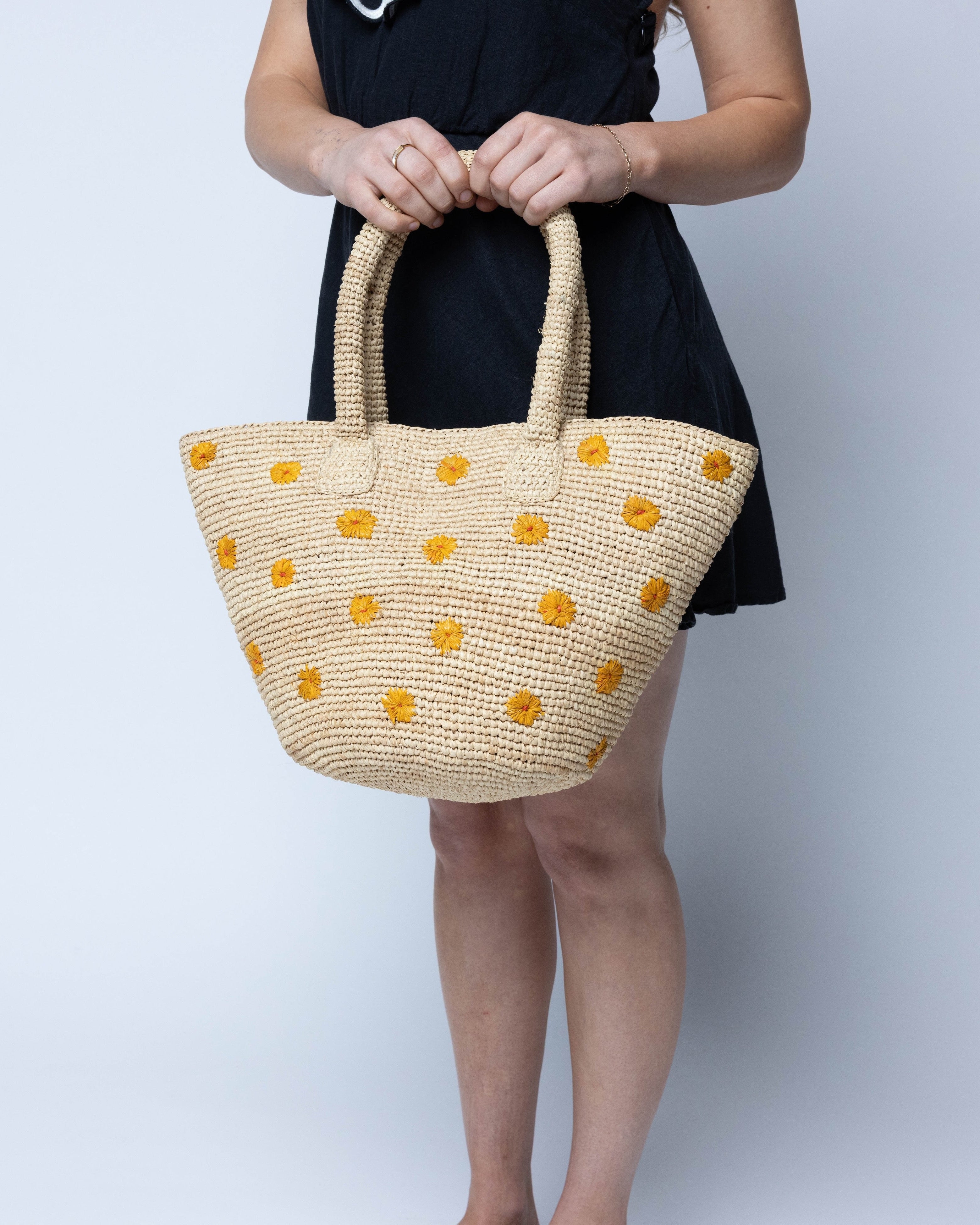 Model wearing Kirra Daisy Flowers Crochet Straw Basket Handbag handmade crochet raffia palm fiber in a solid hue of natural straw color with embroidered round saffron yellow/orange petals and coral orange/red inner dot flower pattern purse with matching crochet handles beach bag purse tote - Shebobo