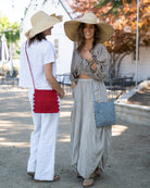 Models wearing Kristen Crochet Straw Crossbody Bag with Nub Edge handmade crochet natural raffia palm fiber in solid hues with two textures of fans and links that create a horizontal stripe pattern across the bag with braided shoulder strap and crochet nub edging along the vertical sides of the purse - Shebobo (with Audrey Big Bow Wide Brim Packable Straw Sun Hats and Natasha XL Brim Woven Straw Sun Hats)