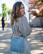 Model wearing Kristen Crochet Straw Crossbody Bag with Nub Edge handmade crochet natural raffia palm fiber in a solid hue of denim retro/light/blue with two textures of fans and links that create a horizontal stripe pattern across the bag with braided shoulder strap and crochet nub edging along the vertical sides of the purse - Shebobo