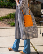 Model wearing Kristen Crochet Straw Crossbody Bag with Nub Edge handmade crochet natural raffia palm fiber in a solid hue of saffron yellow/orange with two textures of fans and links that create a horizontal stripe pattern across the bag with braided shoulder strap and crochet nub edging along the vertical sides of the purse - Shebobo