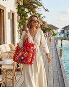 Model wearing Leo Crochet Granny Square Pattern Handbag with Fringe Edge handmade woven raffia palm fiber in a red, cappuccino light brown, seafoam green, blue, coral red/orange, yellow, lime green, pink, black, natural straw color, etc. multicolor pattern of woven granny squares oriented on the diagonal with natural raw fringe edging and handles basket bag - Shebobo