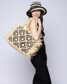 Model wearing Leo Crochet Granny Square Pattern Handbag with Fringe Edge handmade woven raffia palm fiber in a two tone black and natural straw color multicolor pattern of woven granny squares oriented on the diagonal with natural raw fringe edging and handles basket bag - Shebobo
