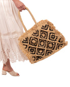 Model wearing Leo Crochet Granny Square Pattern Handbag with Fringe Edge handmade woven raffia palm fiber in a two tone black and natural straw color multicolor pattern of woven granny squares oriented on the diagonal with natural raw fringe edging and handles basket bag - Shebobo