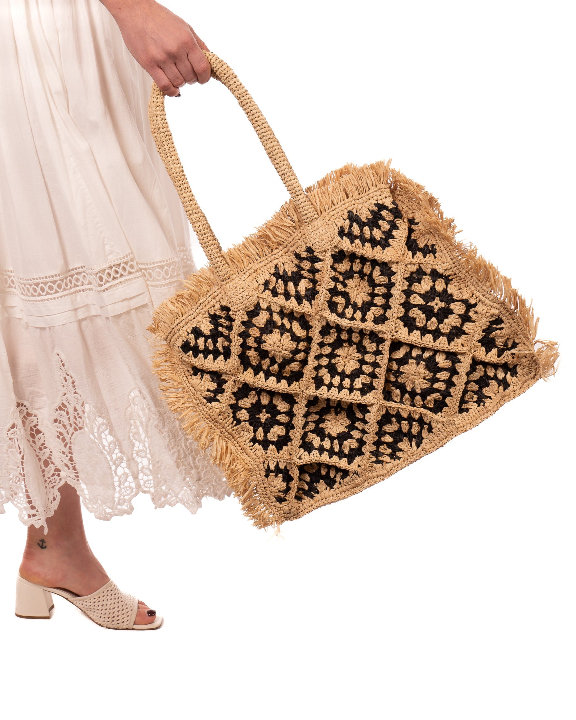 Model wearing Leo Crochet Granny Square Pattern Handbag with Fringe Edge handmade woven raffia palm fiber in a two tone black and natural straw color multicolor pattern of woven granny squares oriented on the diagonal with natural raw fringe edging and handles basket bag - Shebobo