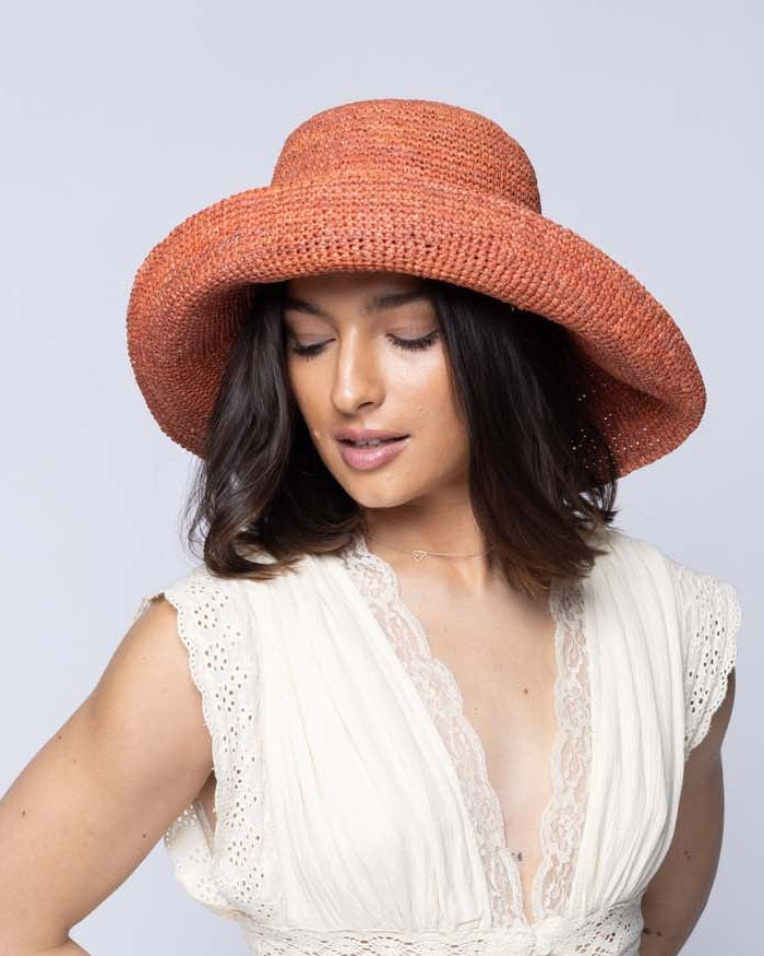 Model wearing Leor Blush crochet straw hat handmade woven natural raffia palm fiber in a solid hue of blush pink/orange raffia 3" brim packable straw hat with matching adjustable braided hat band - Shebobo