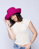 Model wearing Leor Fuchsia crochet straw hat handmade woven natural raffia palm fiber in a solid hue of fuchsia hot/bright/barbie/pink raffia 3" brim packable straw hat with matching adjustable braided hat band - Shebobo
