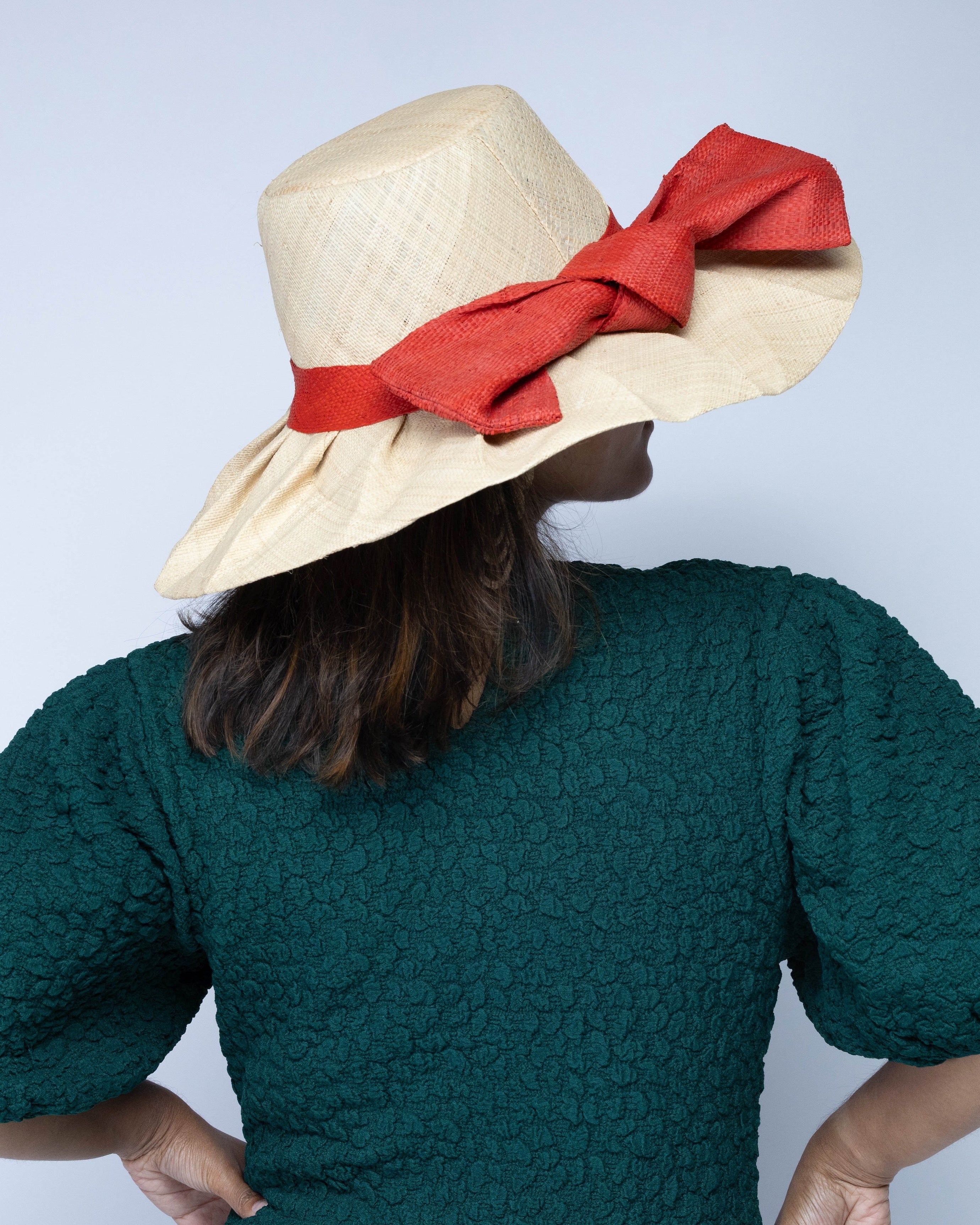 Model wearing Lilly 5" Brim Fan Straw Sun Hat with Big Coral orange/red bow and matching hatband on handmade natural loomed raffia pleated wide brim hat - Shebobo