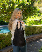 Model wearing Luca Macrame Diamonds Crochet Straw Handbag handmade knotted natural raffia palm fiber in a solid hue of Black in a multi-texture circular pattern of concentric spiral links on the base, cross-hatch x pattern up 2/3rds of the bag, and geometric diamond flower pattern around the top third, with diamond pattern on the base of the shoulder strap handles with tubular loop handle tops - Shebobo