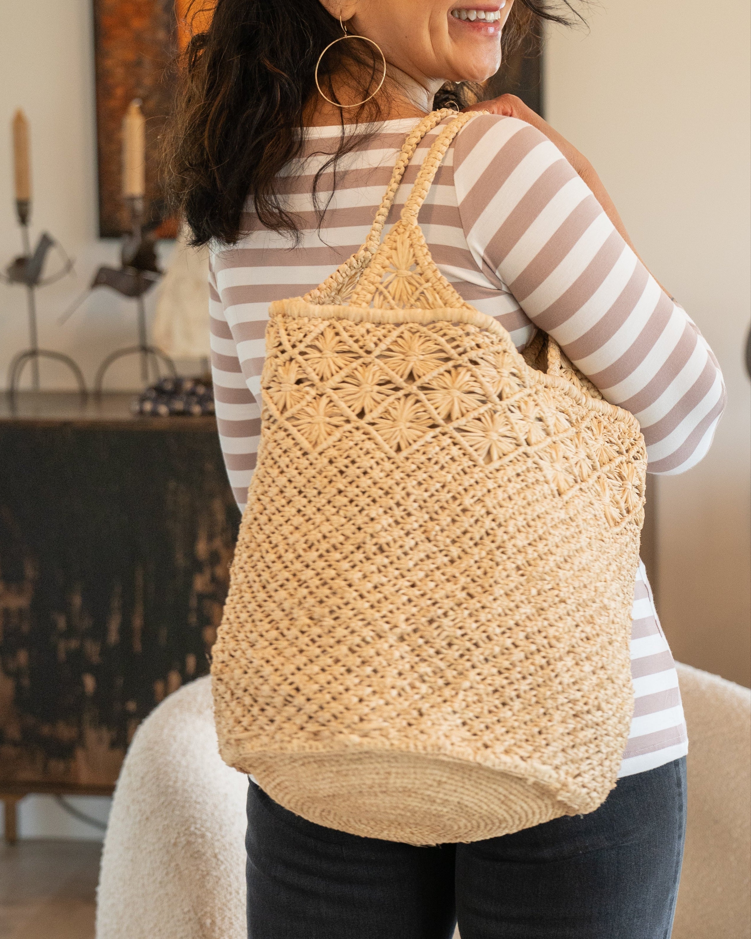 Model wearing Luca Macrame Diamonds Crochet Straw Handbag handmade knotted natural raffia palm fiber in a solid hue of Natural straw color  in a multi-texture circular pattern of concentric spiral links on the base, cross-hatch x pattern up 2/3rds of the bag, and geometric diamond flower pattern around the top third, with diamond pattern on the base of the shoulder strap handles with tubular loop handle tops - Shebobo